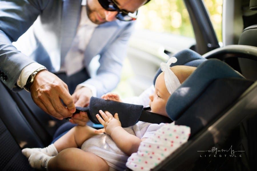 man putting baby girl in the car. Father fastening seat harness of infant car seat