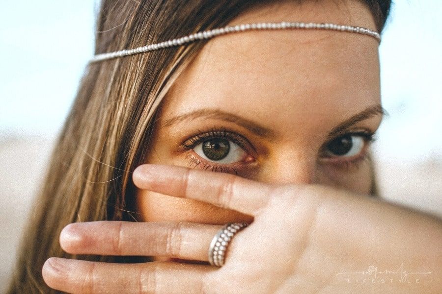 woman with wearing ring and beaded headband covering face beneath eyes with her hand