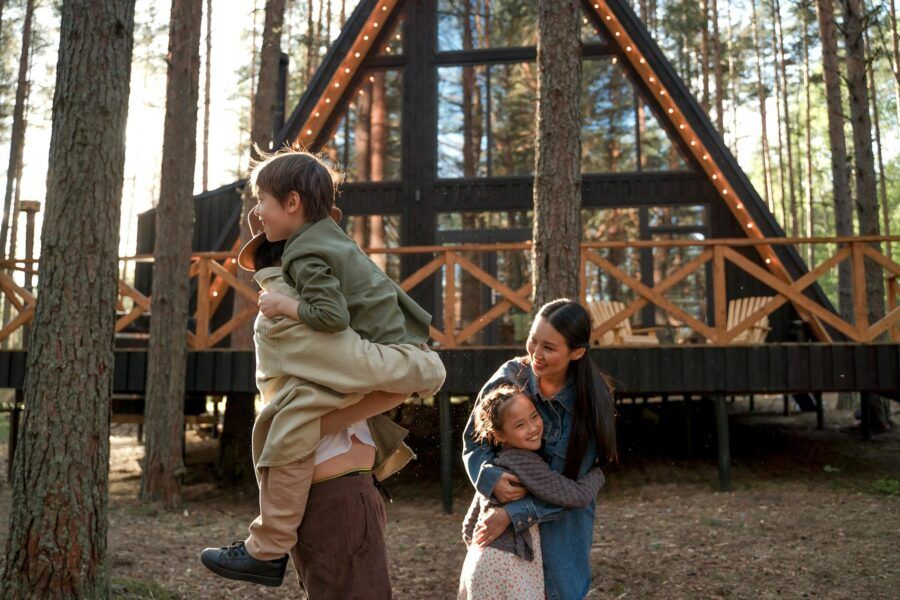 Happy family playing near a stylish A-frame cabin in a forest, enjoying outdoor time.