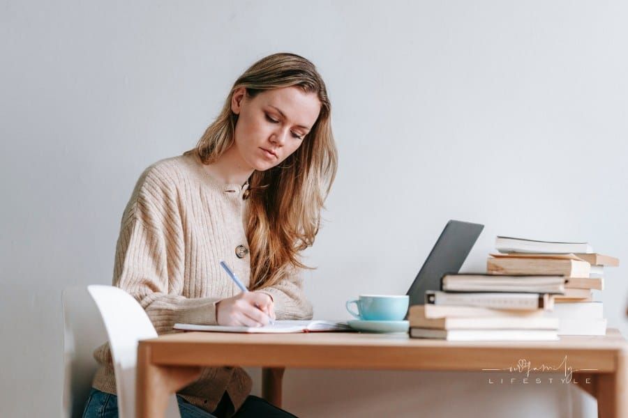 Serious woman writing ideas in notebook near laptop and books