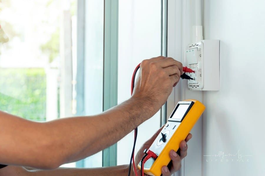 Electrician using a digital meter to measure the voltage at a wall socket on the wall.