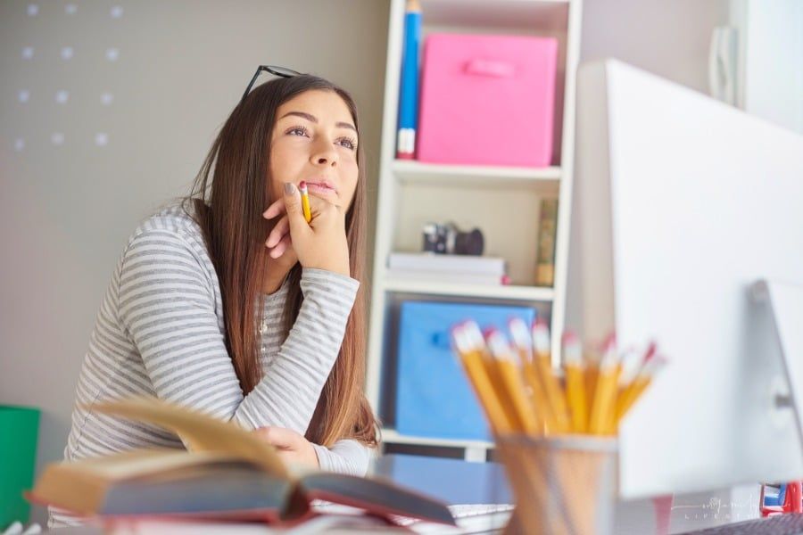 college student daydreaming with glasses on her head and pencil in hand while sitting at her desk