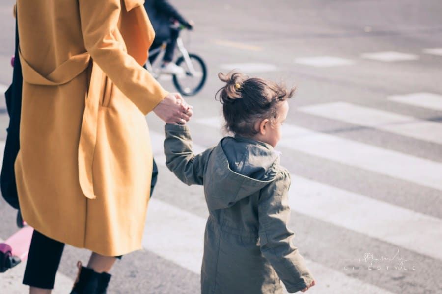 Small girl holding mother's hand on zebra crossing. Mother guiding her daughter while walking a cross the street.
