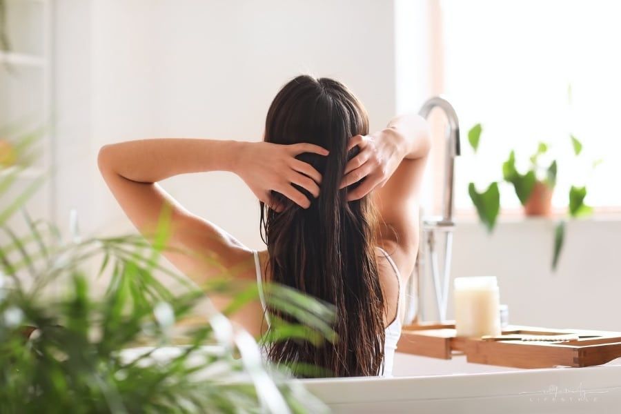 woman applying coconut oil to her hair in the bathroom