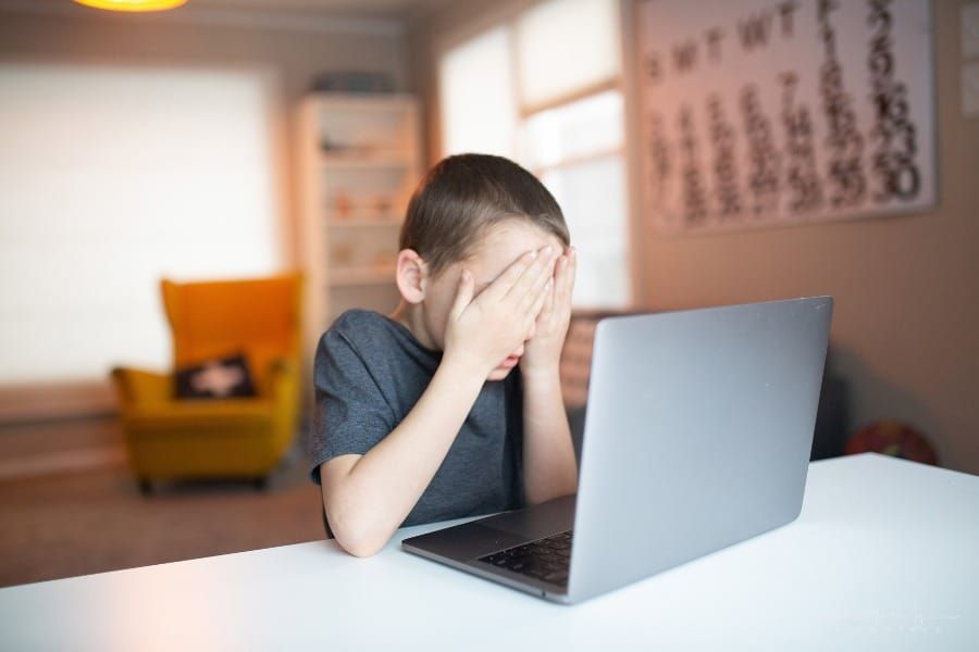 boy covering his eyes while looking at laptop