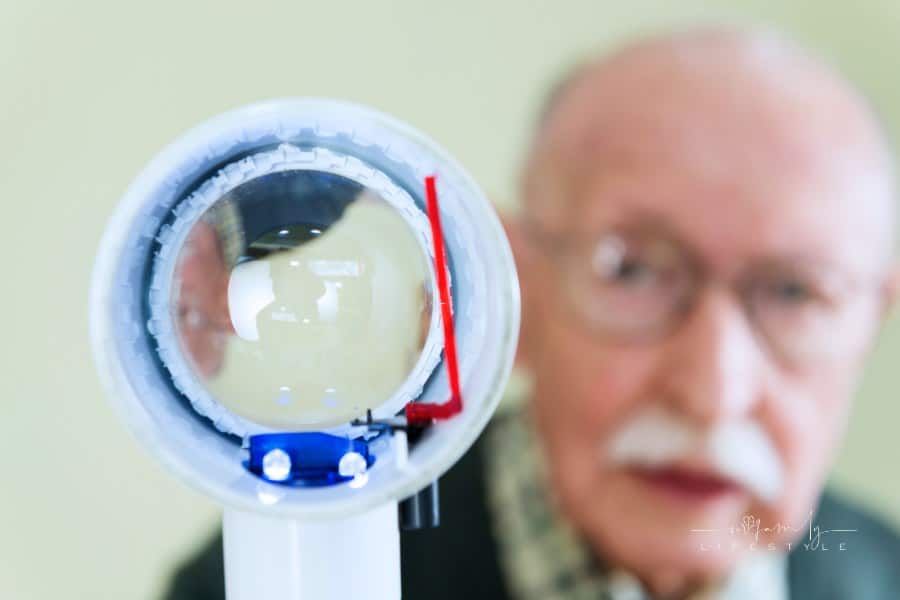Senior man holding an illuminated magnifying glass he uses to help him read because he suffers from Wet Macular Degeneration.