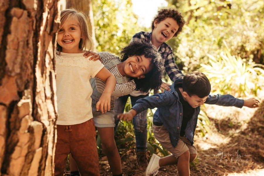 Cute smiling kids peeking out from behind the tree in the park. Group of children enjoying playing hide and seek in a forest.