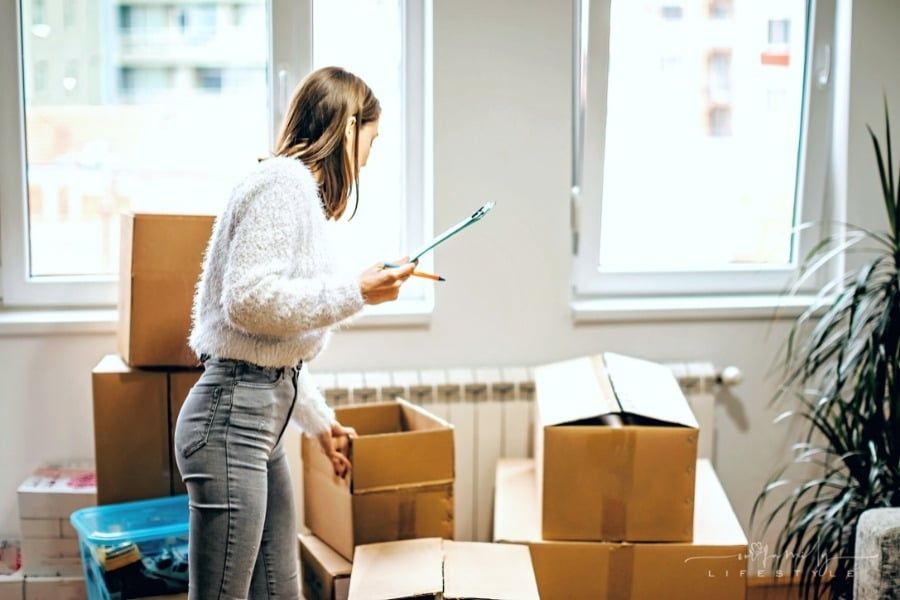 young woman with checklist packing moving boxes