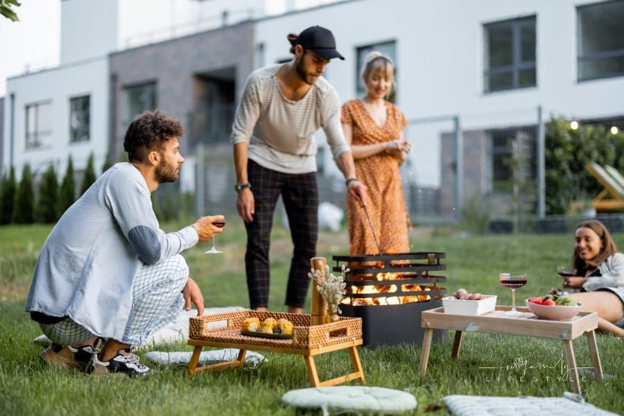 Friends have a picnic, making fire at barbeque and talking on the green lawn at backyard of the country houses on the evening
