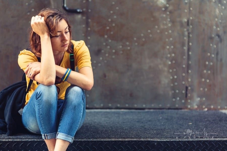 depressed teen girl sitting on sidewalk and holding her head in her hands