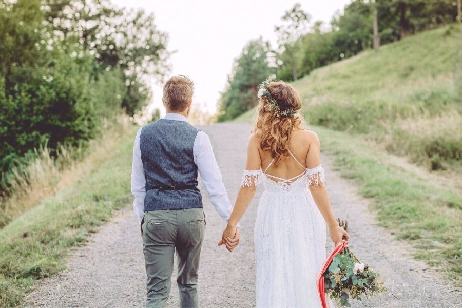 bride carrying bouquet at her side with groom holding her hand on the other walking up gravel road