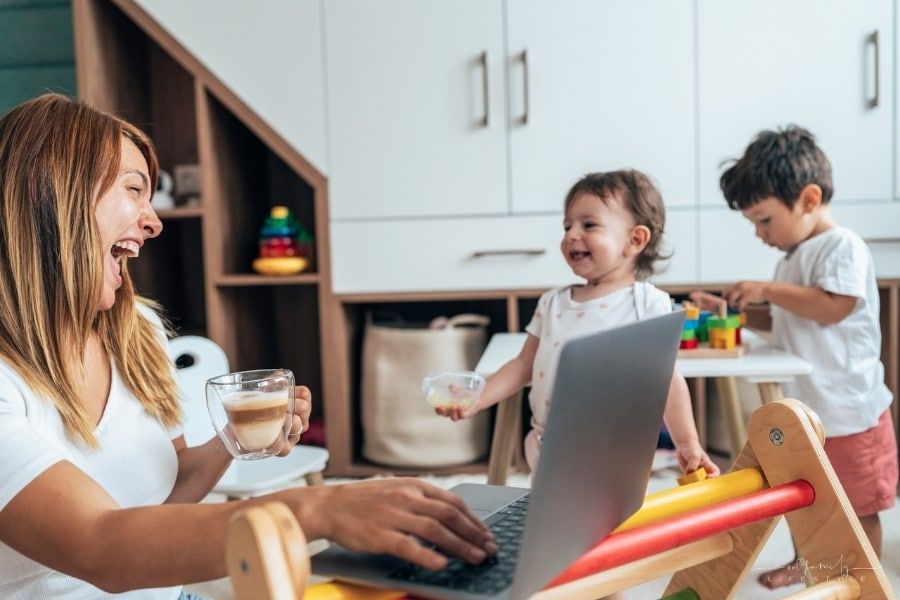 mom with wo small children working on laptop while they play nearby