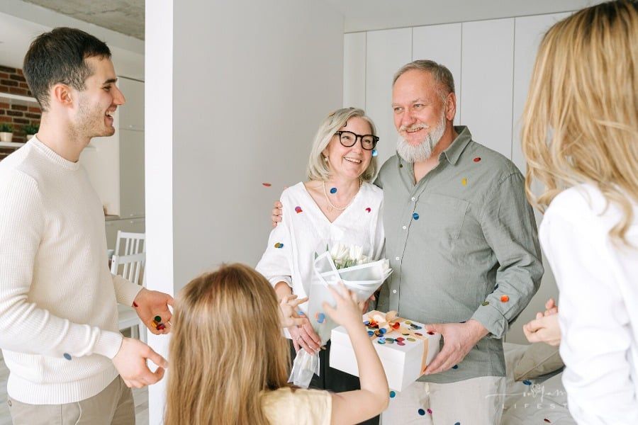 senior couple holding gifts while being showered with confetti from family