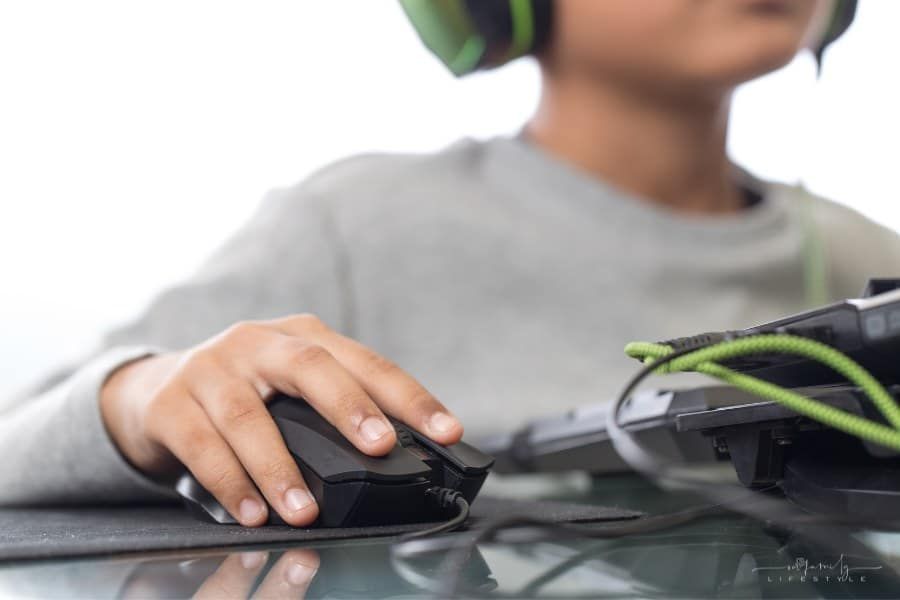 child with hand on mouse and wearing headphones while playing video game on computer
