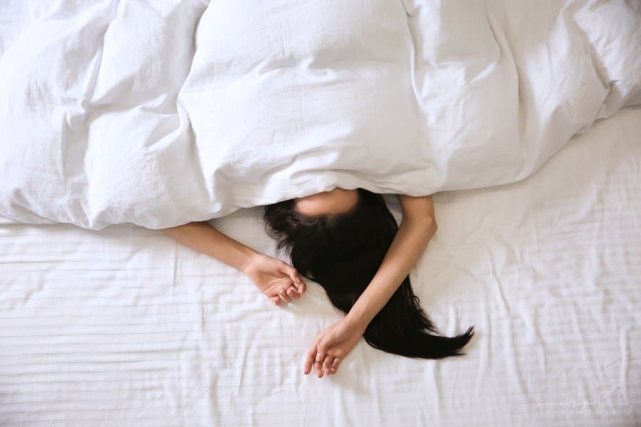 woman laying under blanket with head covered and arms over her head