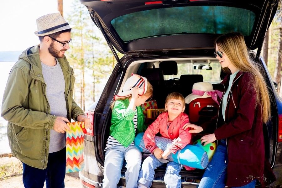 mother and father with two young daughters sitting in back of car while taking a break on a family road trip