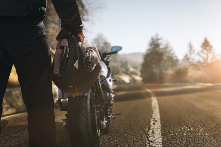 motorcycle rider holding helmet standing behind bike