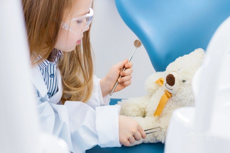 Little cute girl in white doctor robe uniform and protective glasses is treating with instruments, tools her patient bear toy