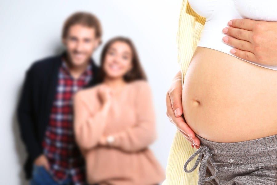 Young Woman in Warm Sweater and Man Wearing Knitted Cardigan behind pregnant surrogate