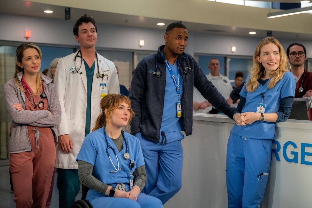 The ensemble cast of Pulse on Netflix stands together in scrubs at the nurses' station.