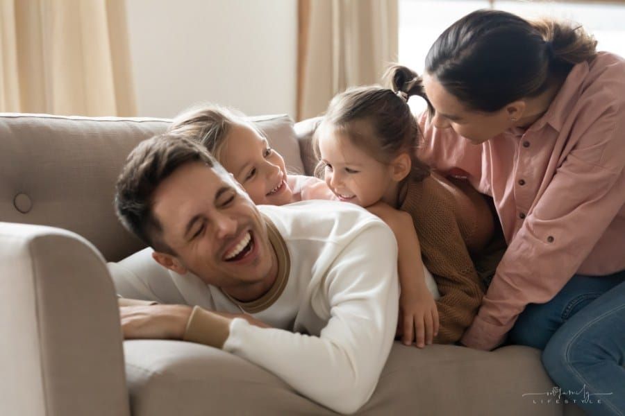 Cheerful happy parents laughing playing with small adorable kids on couch, smiling mom dad and cute children having fun
