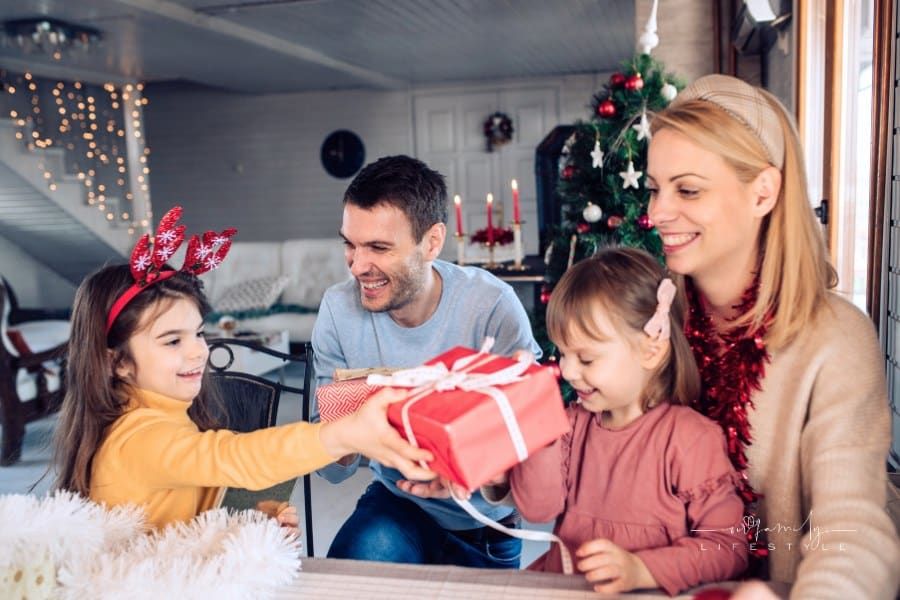 Happy family exchanging Christmas gifts, big sister giving gift to little sister