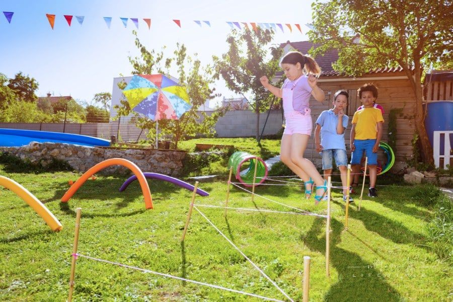Girl jumps in over strings in sequence of obstacles game on playground in a group of kids