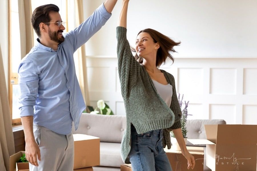 couple celebrating buying new home by dancing around moving boxes