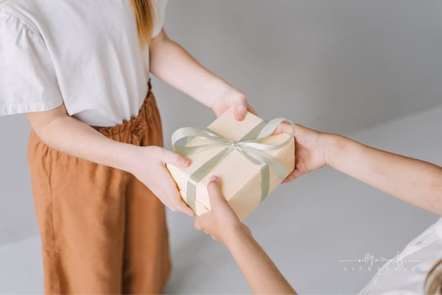 two sets of hands Holding Box with green Ribbon