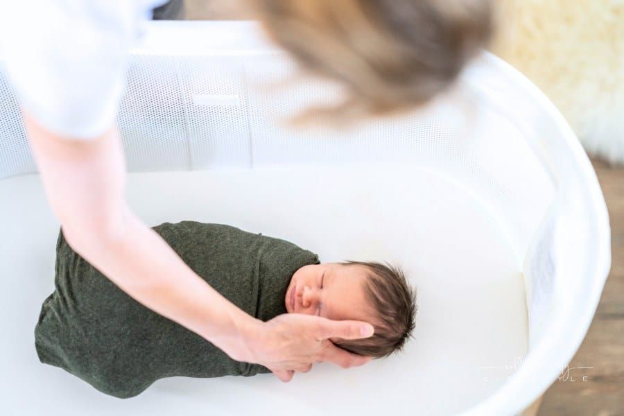 Mother looking down at newborn baby swaddled in bassinet
