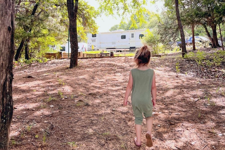toddler walking in dirt to camping spot with rv travel trailer in background