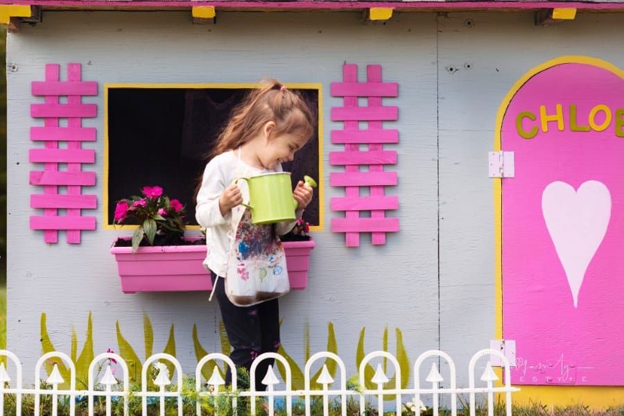little girl gardening arond her wooden playhouse