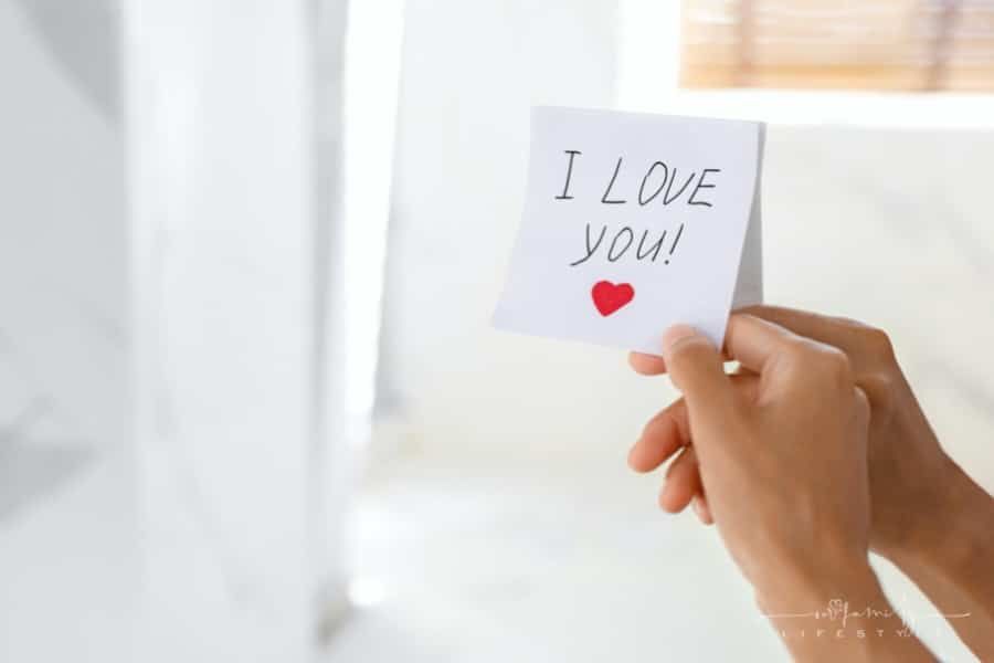 woman's hands holding a love note stuck on mirror