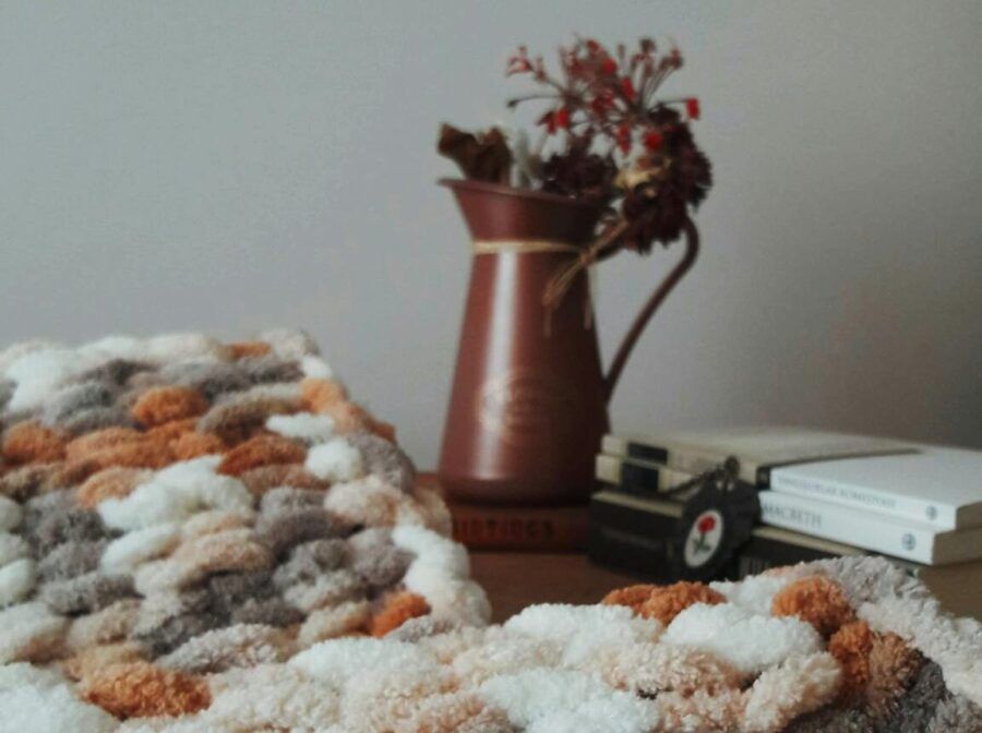 Warm knitted blanket with textured pattern beside a decorative vase on a wooden table.