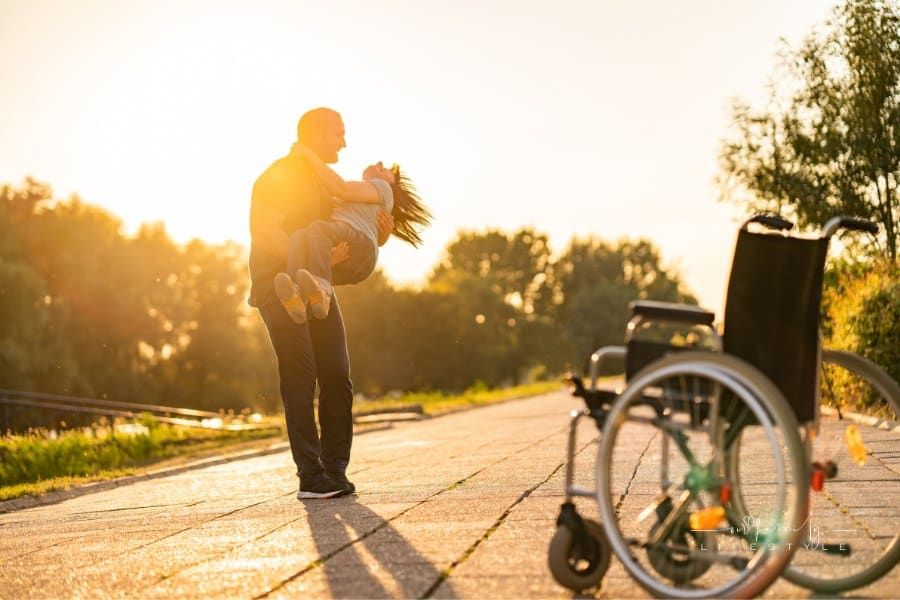 man twirling his disabled wife around with joy as her wheelchair sits in foreground