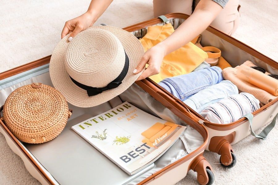 Woman Packing Suitcase with straw hat, clothes, and magazine