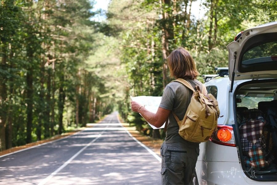 man with backpack looking at map standing beside car on a forest road among trees