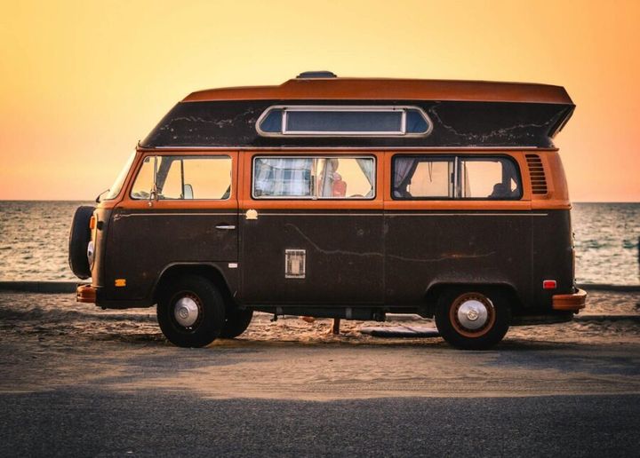 A classic Volkswagen campervan parked by the sea during a vibrant sunset.