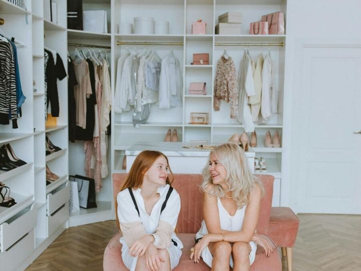 A mother and daughter sit together in a stylish walk-in closet, choosing shoes.