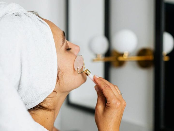 A woman using a face roller for a skincare routine in a bathroom setting.