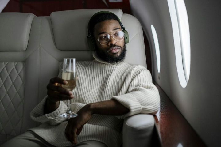 African American man relaxing in a private jet, sipping champagne and listening to music.