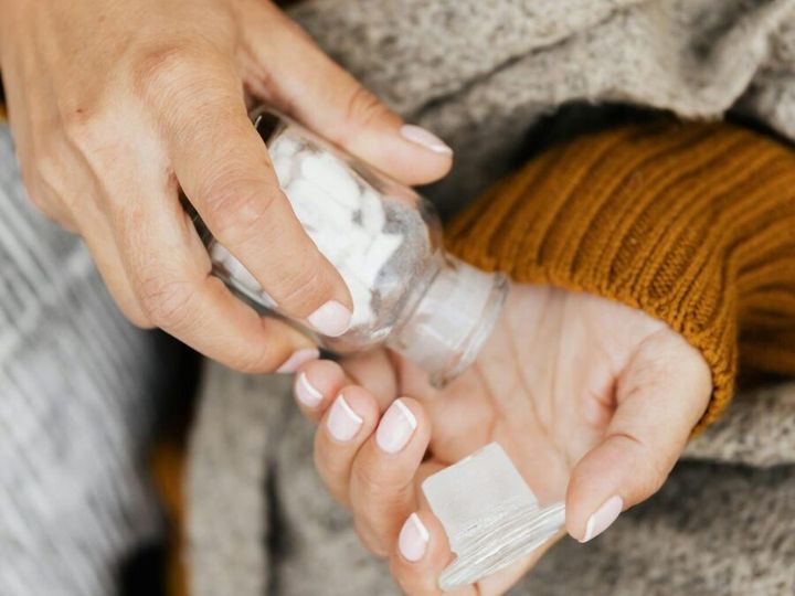 Close-up of a woman in a knitted sweater holding and pouring pills from a glass bottle indoors.