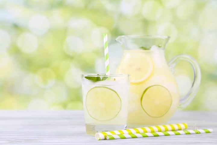 homemade lemonade in a glass and pitcher with lemon slices on a table