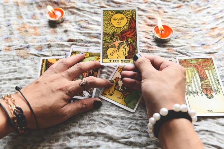 fortune teller's hands holding tarot cards over candellit table
