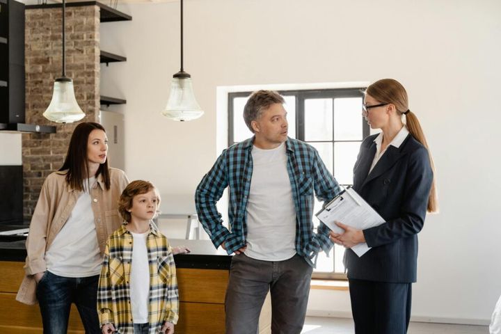 Family with child talks to real estate agent in modern kitchen during home showing.