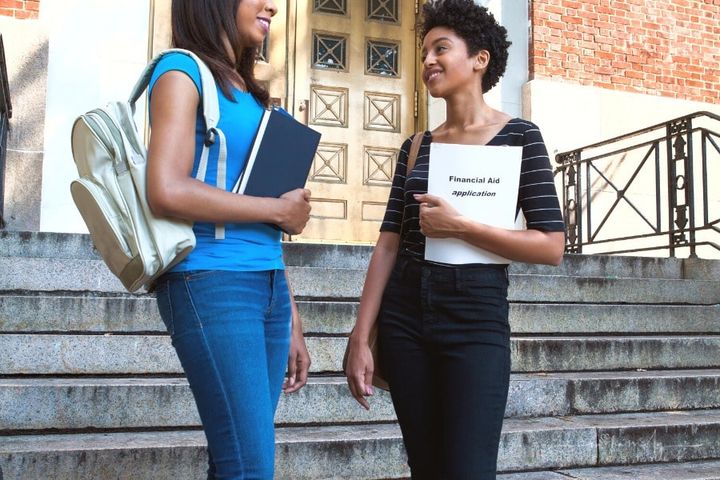 two students standing in front of building entrance with one holding financial aid application