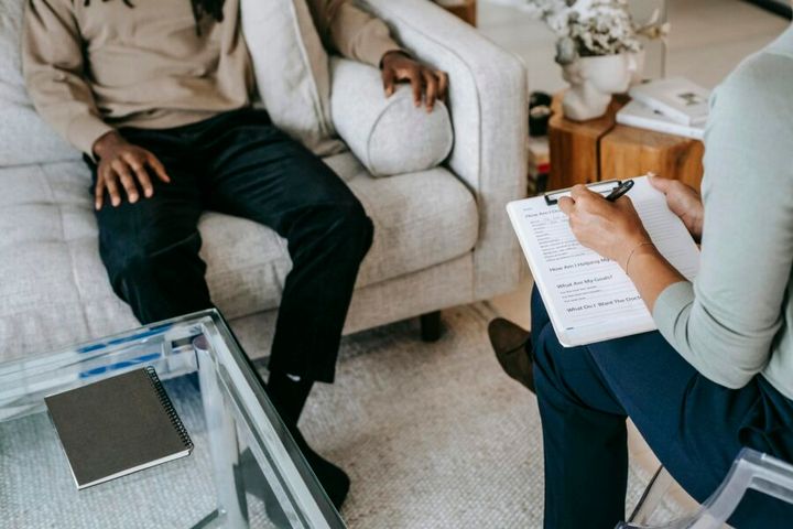 From above crop African American male in casual clothes sitting on comfy couch and answering professional female consultant q