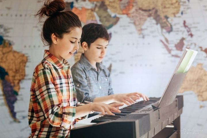 brother and sister playing keyboard in front of wall map
