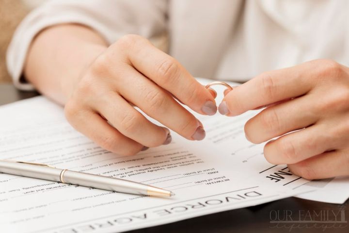 hands holding wedding ring over divorce papers