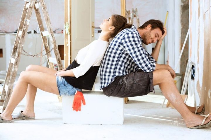 Exhausted couple sitting back-to-back in house under construction